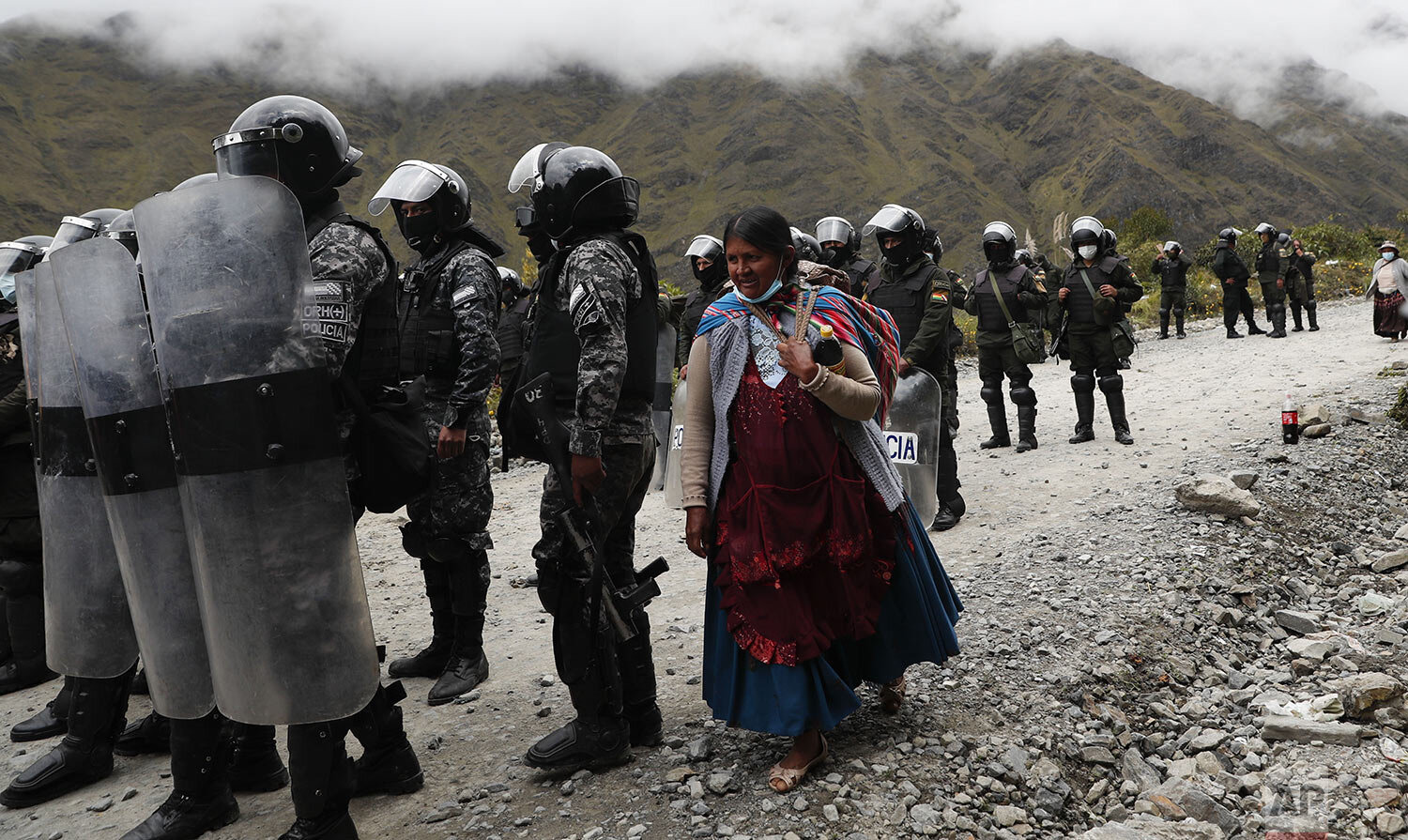 A woman walks past police who dispersed coca farmers in Unduavi, Bolivia, March 16, 2021. The farmers blocked traffic to protest the relocation of the coca market and a court ruling recognizing a new leader of the Coca Producers Association. (AP Pho