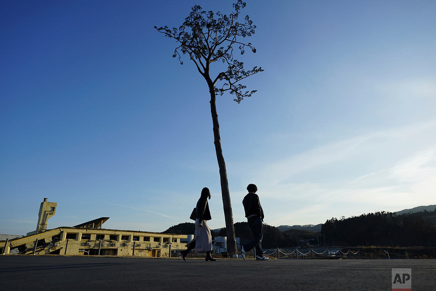  A man and a woman walk near a replica of a lone pine tree that initially survived the 2011 tsunami that flattened the surrounding coastal forest, in Rikuzentakata, Iwate Prefecture, northern Japan Thursday, March 4, 2021. The tree, which eventually 