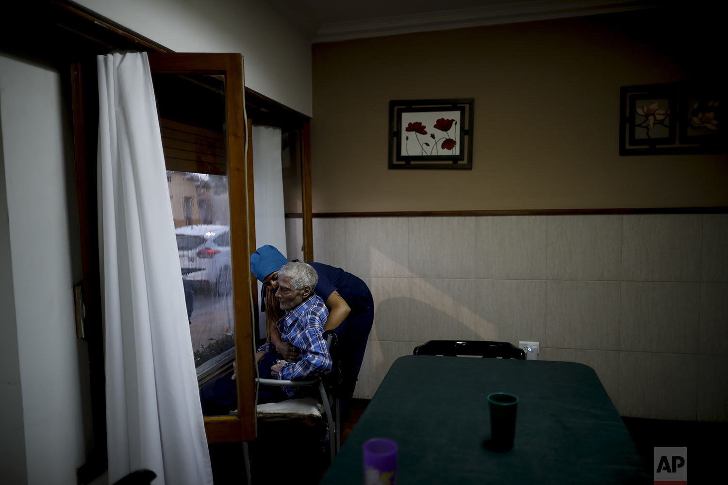  Nurse Rocio Lescano, 86, helps Victor Tripiana in his chair in front of a window where he visits with his family on the other side, at the Reminiscencias residence in Tandil, Argentina, Sunday, April 4, 2021. (AP Photo/Natacha Pisarenko) 