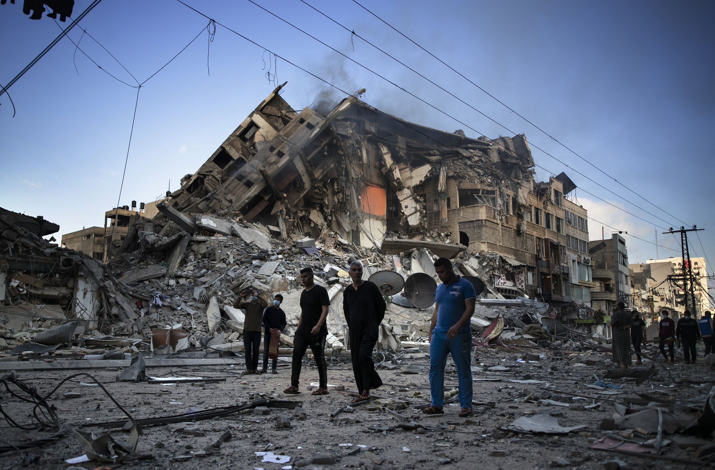  Palestinians walk next to the remains of a destroyed 15 story building after being hit by Israeli airstrikes on Gaza City, Thursday, May 13, 2021. (AP Photo/Khalil Hamra) 