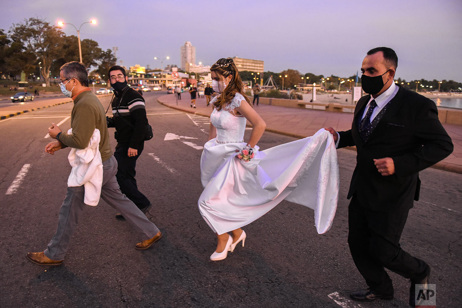  Bride Rocio Silva, from Uruguay, gets help with her dress from her Cuban groom Mario Carrasco as they cross the street with family after a portrait session along the seawall shortly after getting married during the new coronavirus pandemic in Montev