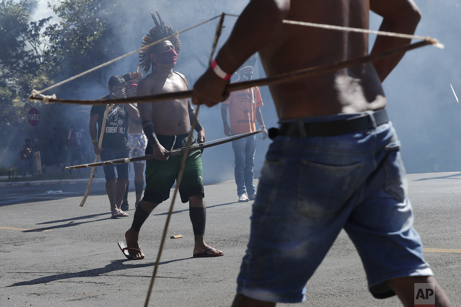  Indigenous men armed with bows and arrows walk amid tear gas fired by police outside Congres where they protest a proposed bill they say would limit recognition of reservation land, in Brasilia, Brazil, June 22, 2021. (AP Photo/Eraldo Peres) 