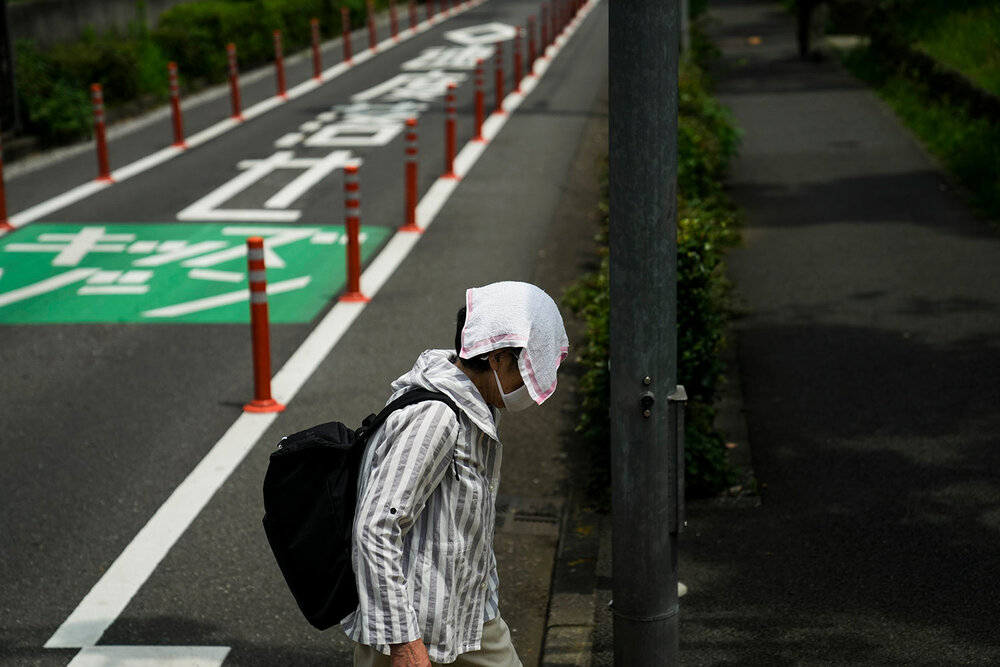  An elderly woman walks with a small towel over her head to shield from the sun ahead the 2020 Summer Olympics, Wednesday, July 14, 2021, in Tokyo. (AP Photo/Jae C. Hong) 