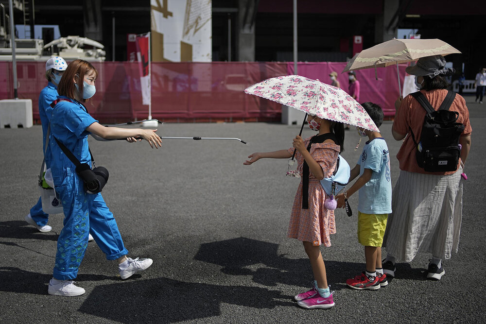  A volunteer sprays water on children as they use umbrellas to beat the heat outside the Fuji International Speedway, the finish for the women's cycling road race that is underway, at the 2020 Summer Olympics, Sunday, July 25, 2021, in Oyama, Japan. 