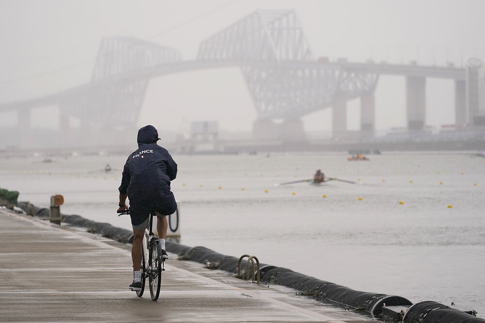  A coach from France rides her bike as rowers train during a rowing training session at the 2020 Summer Olympics, Tuesday, July 27, 2021, in Tokyo, Japan. (AP Photo/Darron Cummings) 