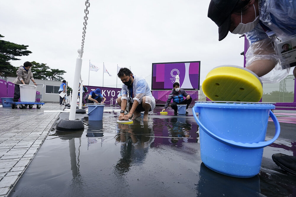  Volunteers attempt to remove the rainwater from the range before the women's trap practice at the Asaka Shooting Range in the 2020 Summer Olympics, Tuesday, July 27, 2021, in Tokyo, Japan. (AP Photo/Alex Brandon) 