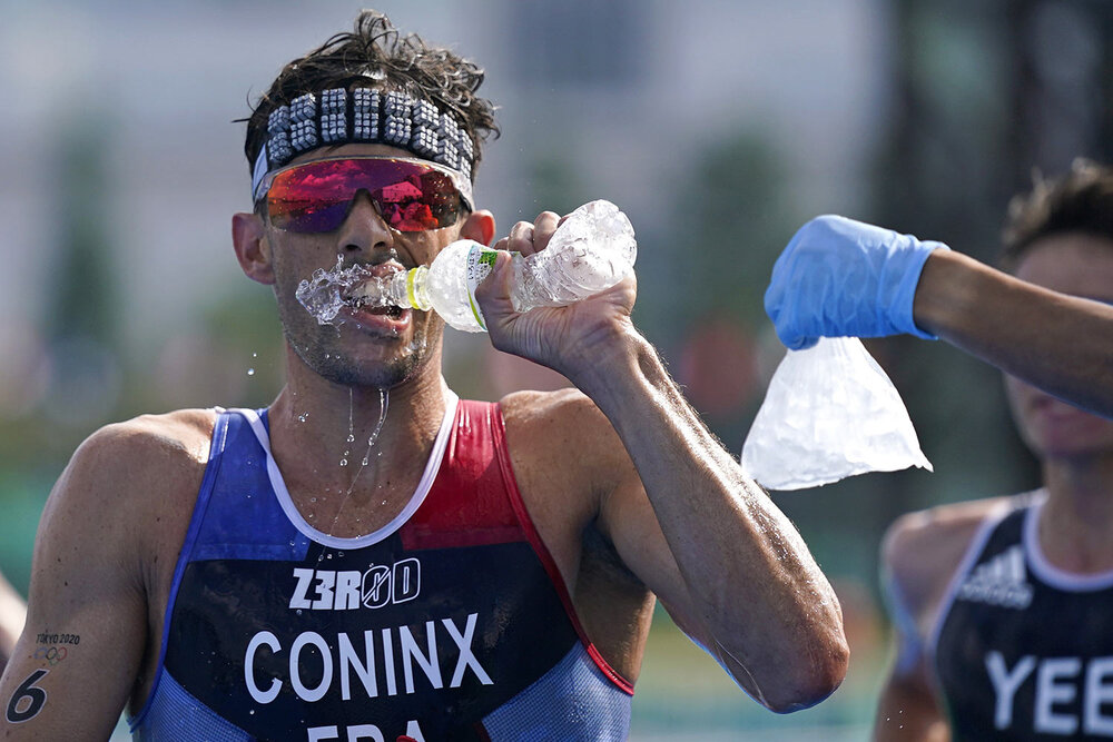  Dorian Coninx of France takes water as a volunteer holds out a bag of ice, during the run portion of the men's individual triathlon at the 2020 Summer Olympics, Monday, July 26, 2021, in Tokyo, Japan. (AP Photo/Jae C. Hong) 