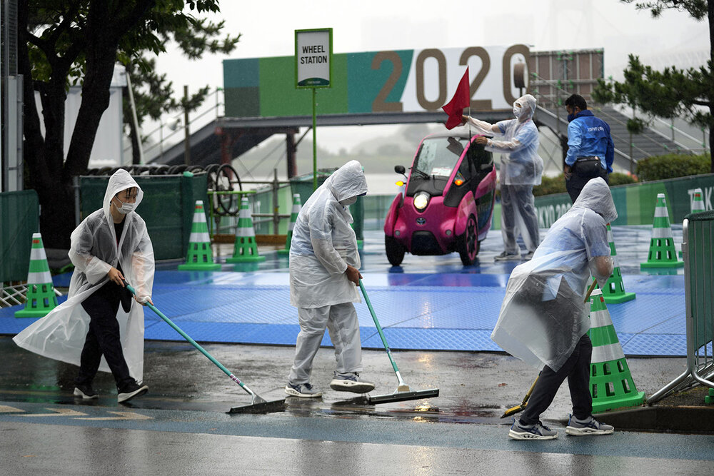  Olympic workers wipe off rain water from the competition site prior to the women's triathlon competition at the 2020 Summer Olympics on Tuesday, July 27, 2021, in Tokyo, Japan. (AP Photo/Eugene Hoshiko) 