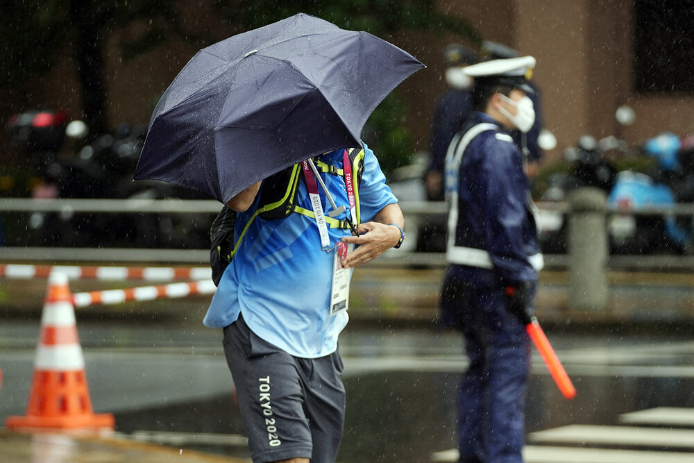  A staff holds an umbrella against strong wind and rain prior to the women's triathlon competition at the 2020 Summer Olympics Tuesday, July 27, 2021, in Tokyo, Japan. (AP Photo/Eugene Hoshiko) 