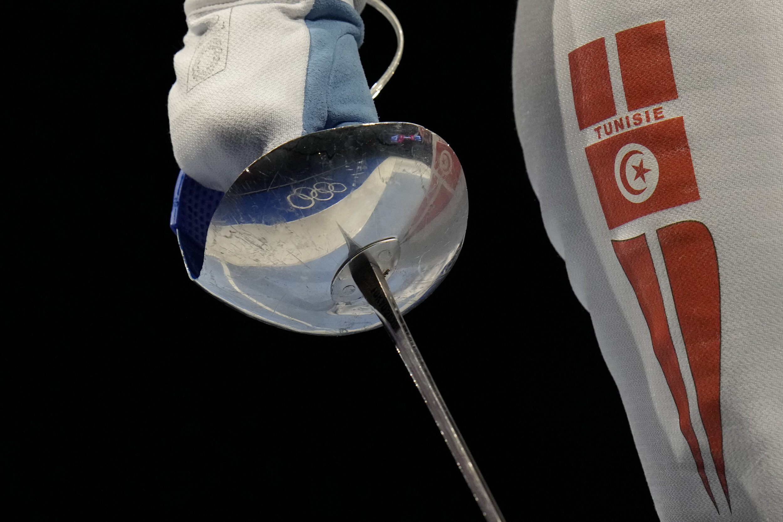  The Olympic rings are reflected on Sabre weapon of Olfa Hezami of Tunisia as competes with Norika Tamura of Japan in the women's Sabre team round of 16 competition at the 2020 Summer Olympics, Saturday, July 31, 2021, in Chiba, Japan. (AP Photo/Hass