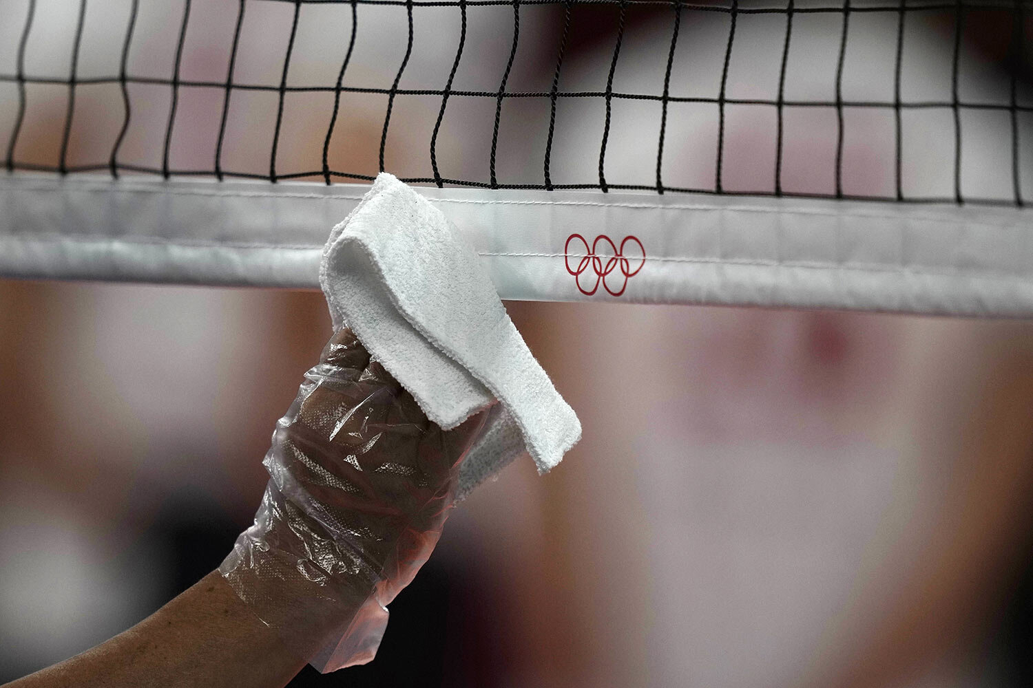  A steward uses a plastic glove and a cloth to disinfect the volleyball net during a rehearsal before the start of the volleyball preliminaries at Ariake Arena at the 2020 Summer Olympics, Friday, July 23, 2021, in Tokyo, Japan. (AP Photo/Frank Augst