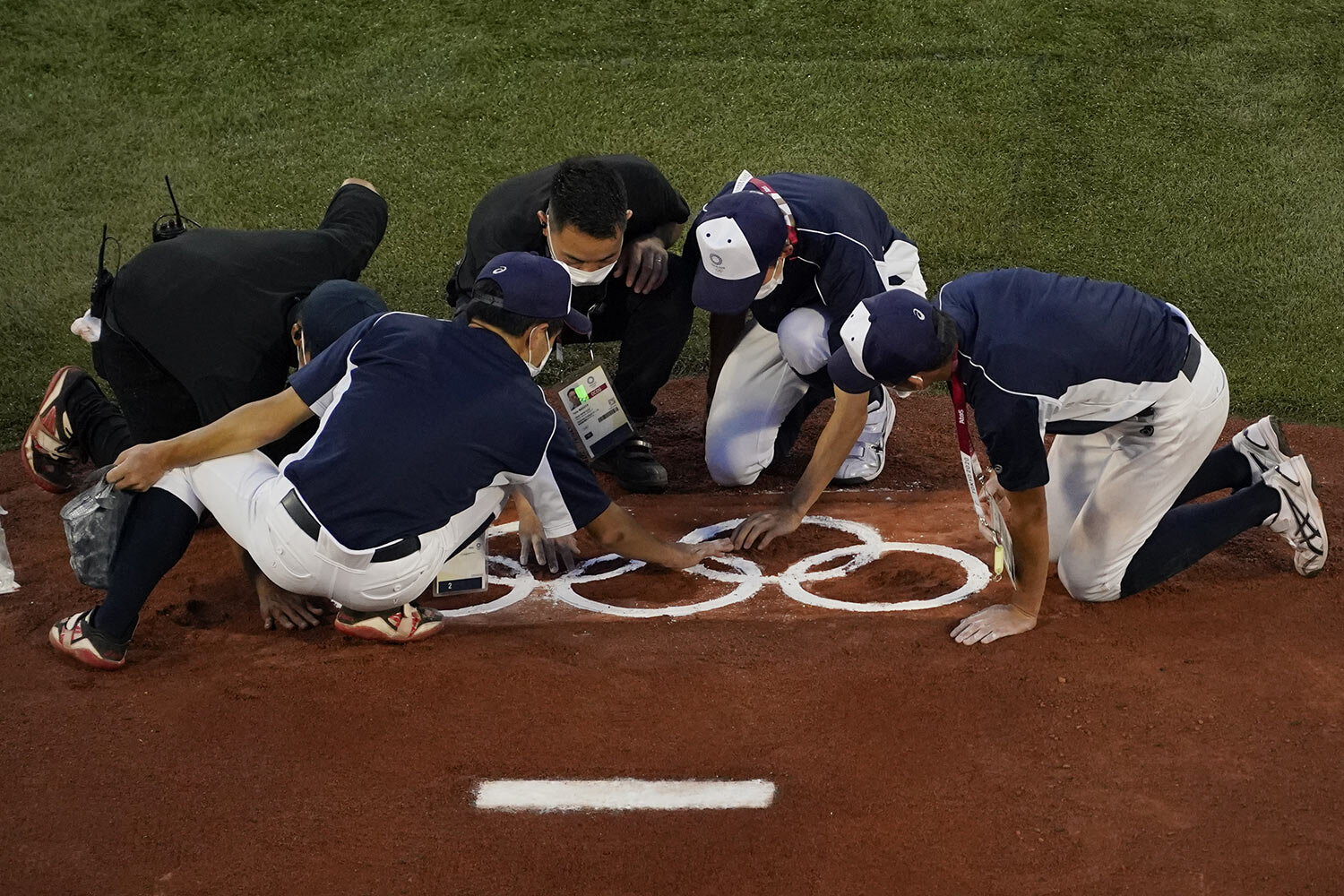  Workers place the Olympic Rings on the pitching mound ahead of a baseball game between The Dominican Republic and South Korea at the 2020 Summer Olympics, Sunday, Aug. 1, 2021, in Yokohama, Japan. (AP Photo/Sue Ogrocki) 