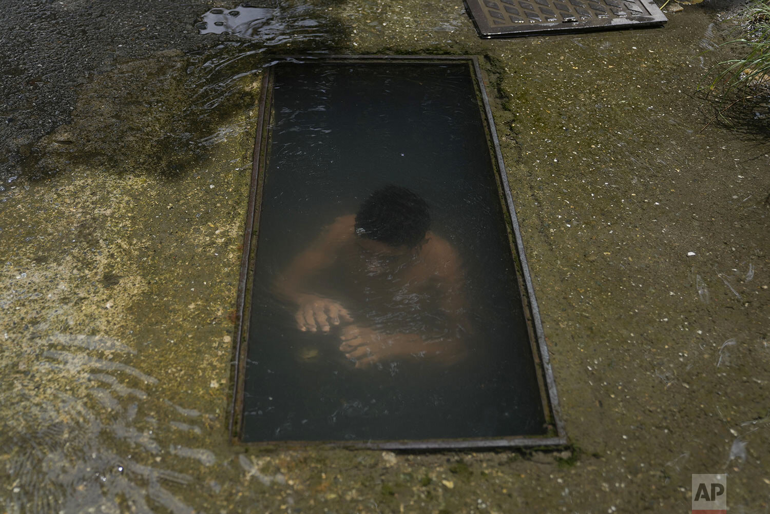  A boy submerges himself to cool down at the site of a broken water main at a street in Caracas, Venezuela, Tuesday, July 27, 2021, amid the new coronavirus pandemic. (AP Photo/Ariana Cubillos) 