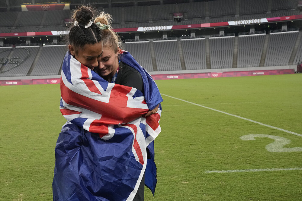  New Zealand's Risi Pouri-Lane, left, and Michaela Blyde hug, wrapped in a national flag, as they celebrate in the empty stadium after receiving their gold medals in women's rugby sevens at the 2020 Summer Olympics, Saturday, July 31, 2021 in Tokyo, 
