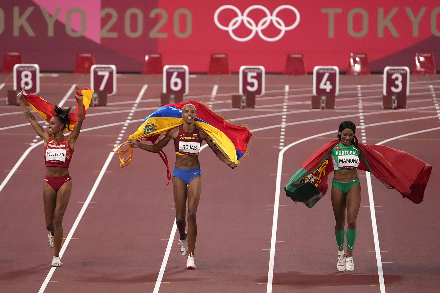 Gold medalist Yulimar Rojas of Venezuela, center, silver medalist Patricia Mamona of Portugal, right, and bronze medalist Ana Peleteiro of Spain, celebrate on the track following the final of the women's triple jump at the 2020 Summer Olympics, Sund