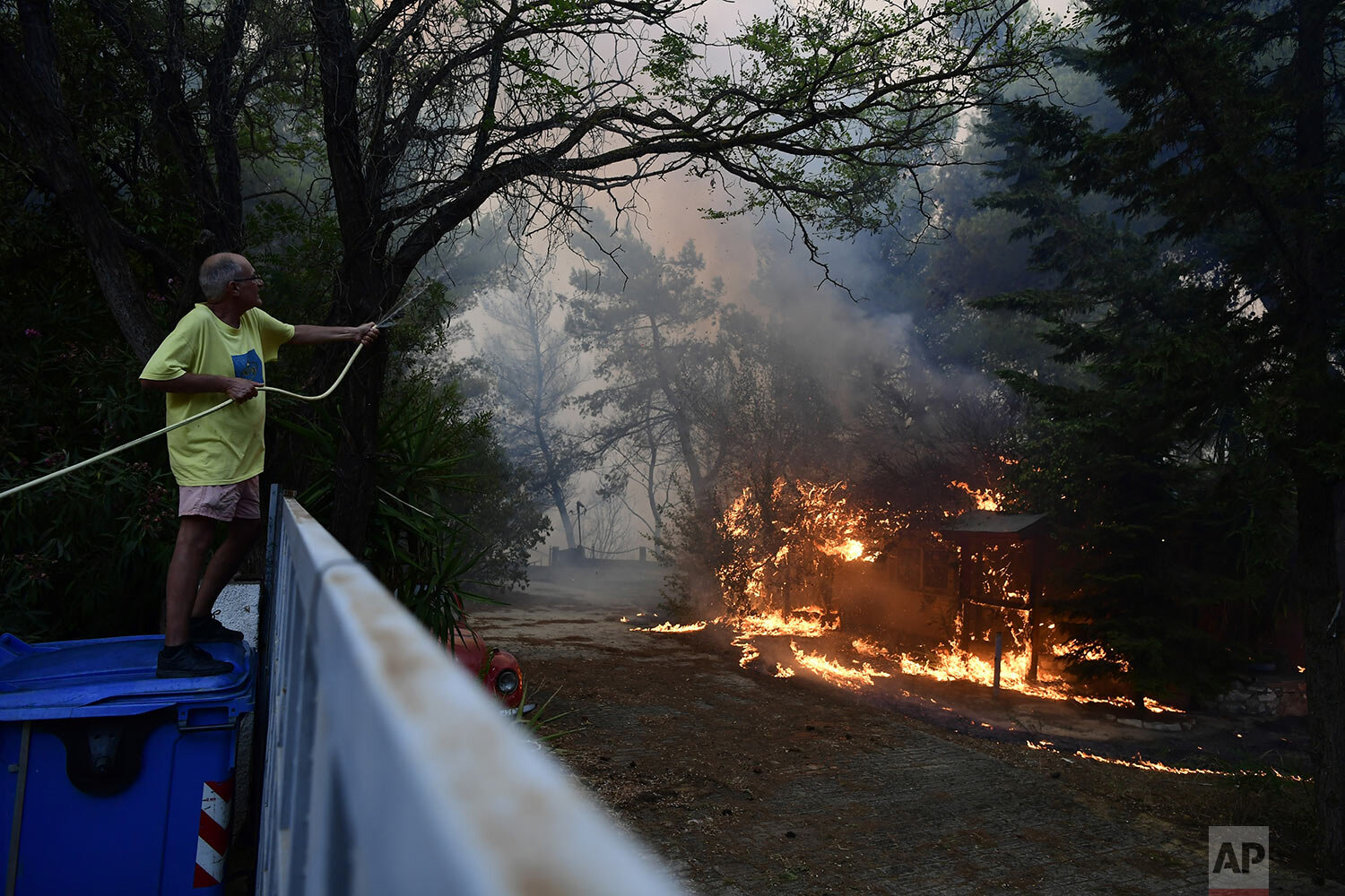  A man drops water to burning trees during a wildfire in Adames area, northern Athens, Greece, Tuesday, Aug. 3, 2021. Hundreds of residents living near a forest area north of Athens fled their homes Tuesday as a wildfire reached residential areas as 