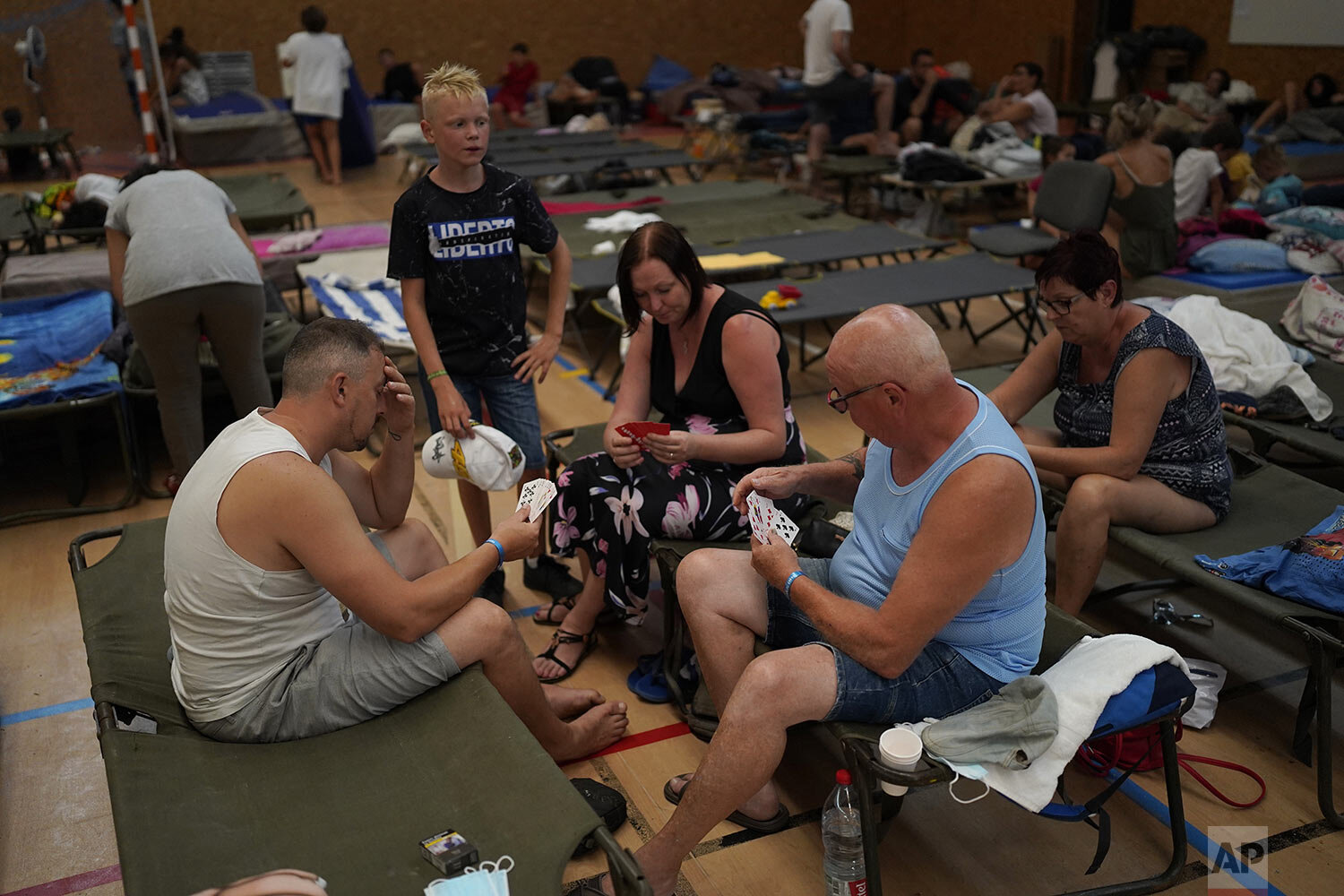  Evacuated campers play cards in a gymnasium in Bormes-les-Mimosas, southern France, Wednesday, Aug. 18, 2021. Firefighters have been able to "stabilize" the blaze that raced Tuesday through forests near the French Riviera, forcing thousands of peopl