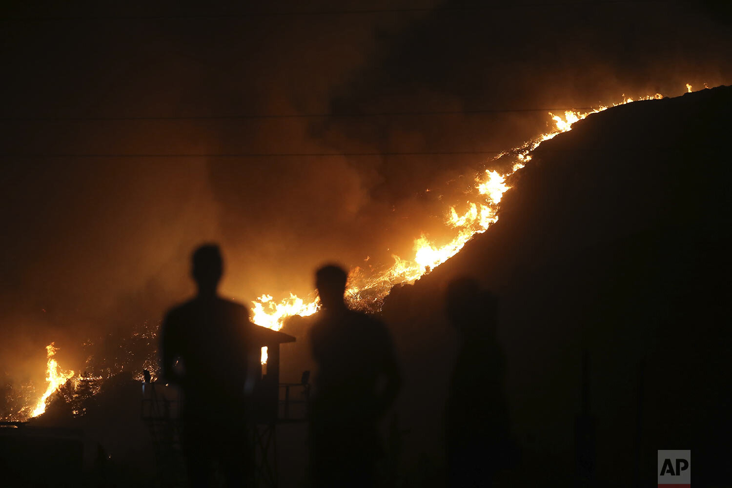  People stand in front of Kemerkoy Thermal Power Plant with the blaze approaching in the background, in Milas, Mugla, Turkey, Tuesday, Aug. 3, 2021. Turkish President Recep Tayyip ErdoganÕs government is facing increased criticism over its apparent p