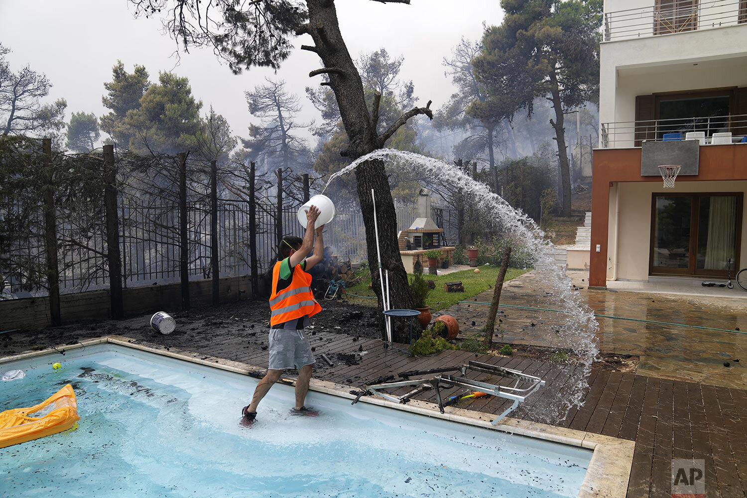  A man throws water from a swimming pool as the fire approaches his house in Ippokratios Politia village, about 35 kilometres (21 miles) north of Athens, Greece, Friday, Aug. 6, 2021. Thousands of people fled wildfires burning out of control in Greec