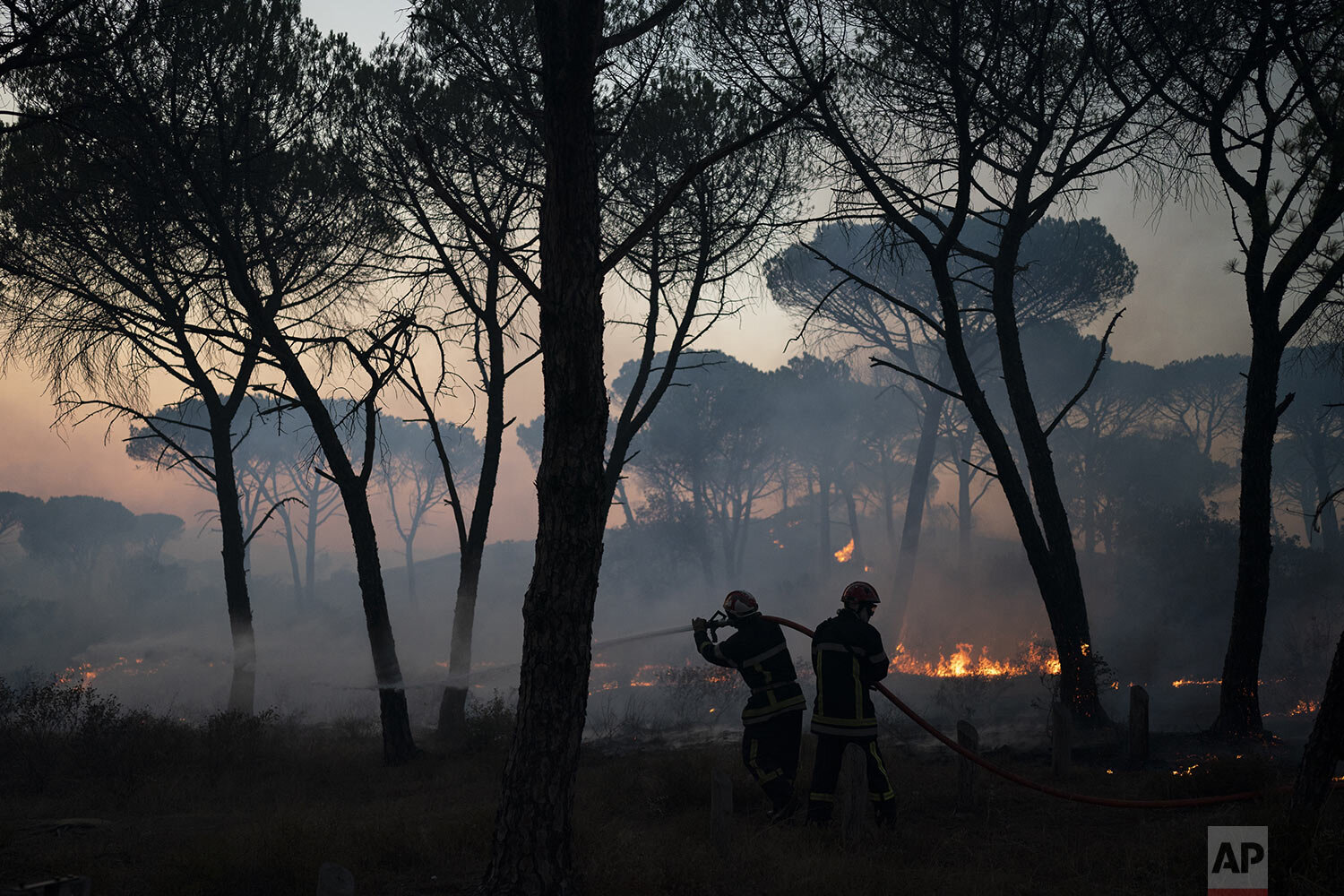  Firemen use a hose to extinguish a fire near Le Luc, southern France, Tuesday, Aug. 17, 2021. Thousands of people fled homes, campgrounds and hotels near the French Riviera on Tuesday as firefighters battled a blaze that raced through nearby forests