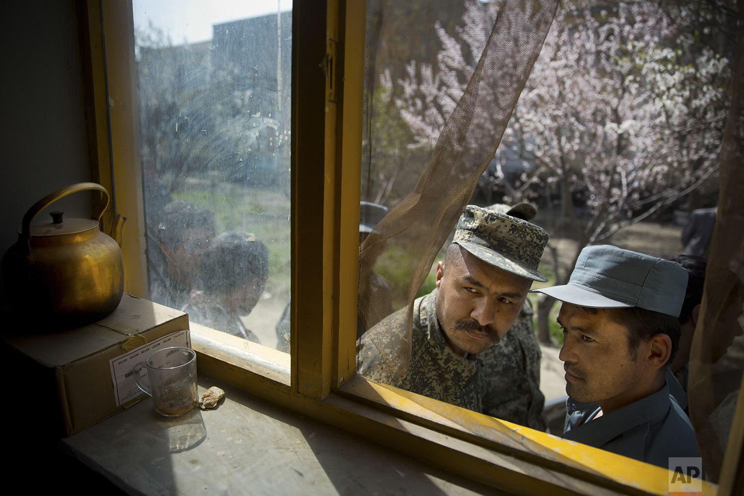  An Afghan soldier, left, and a police man peek through a window as they queue with others to get their registration card on the last day of voter registration for the upcoming presidential elections outside a school in Kabul, Afghanistan, Tuesday, A