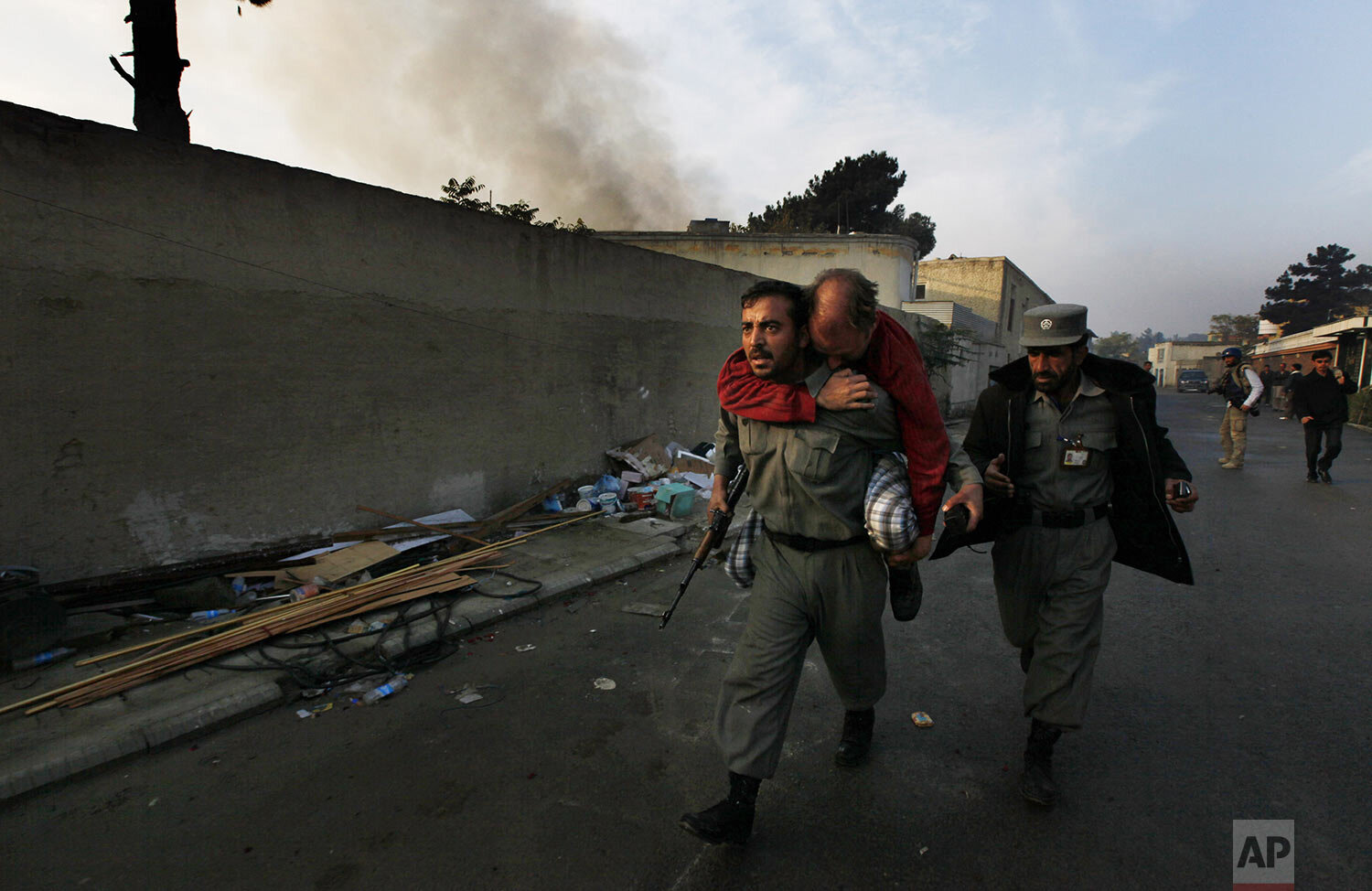  An Afghan police officer carries an injured unidentified German national as smoke bellows from the site of an attack in Kabul, Afghanistan on Wednesday, Oct. 28, 2009. Gunmen attacked a guest house used by U.N. staff in the Afghan capital of Kabul. 