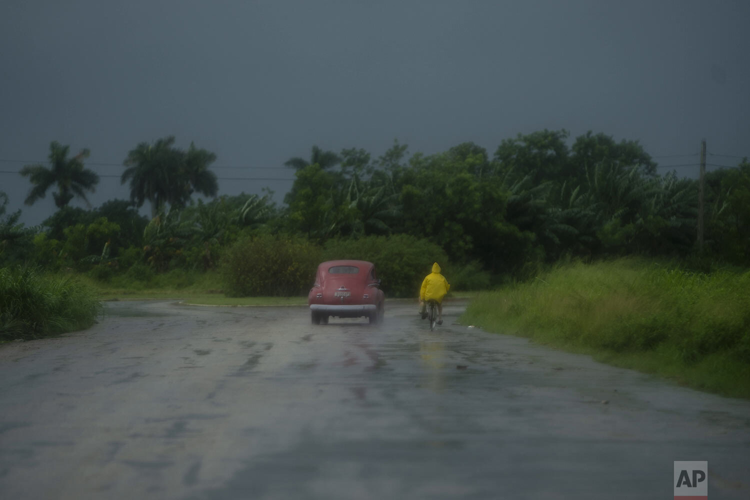  A man rides a bicycle alongside a car in the rain brought by Hurricane Ida, in Guanimar, Artemisa province, Cuba, Aug. 28, 2021. (AP Photo/Ramon Espinosa) 