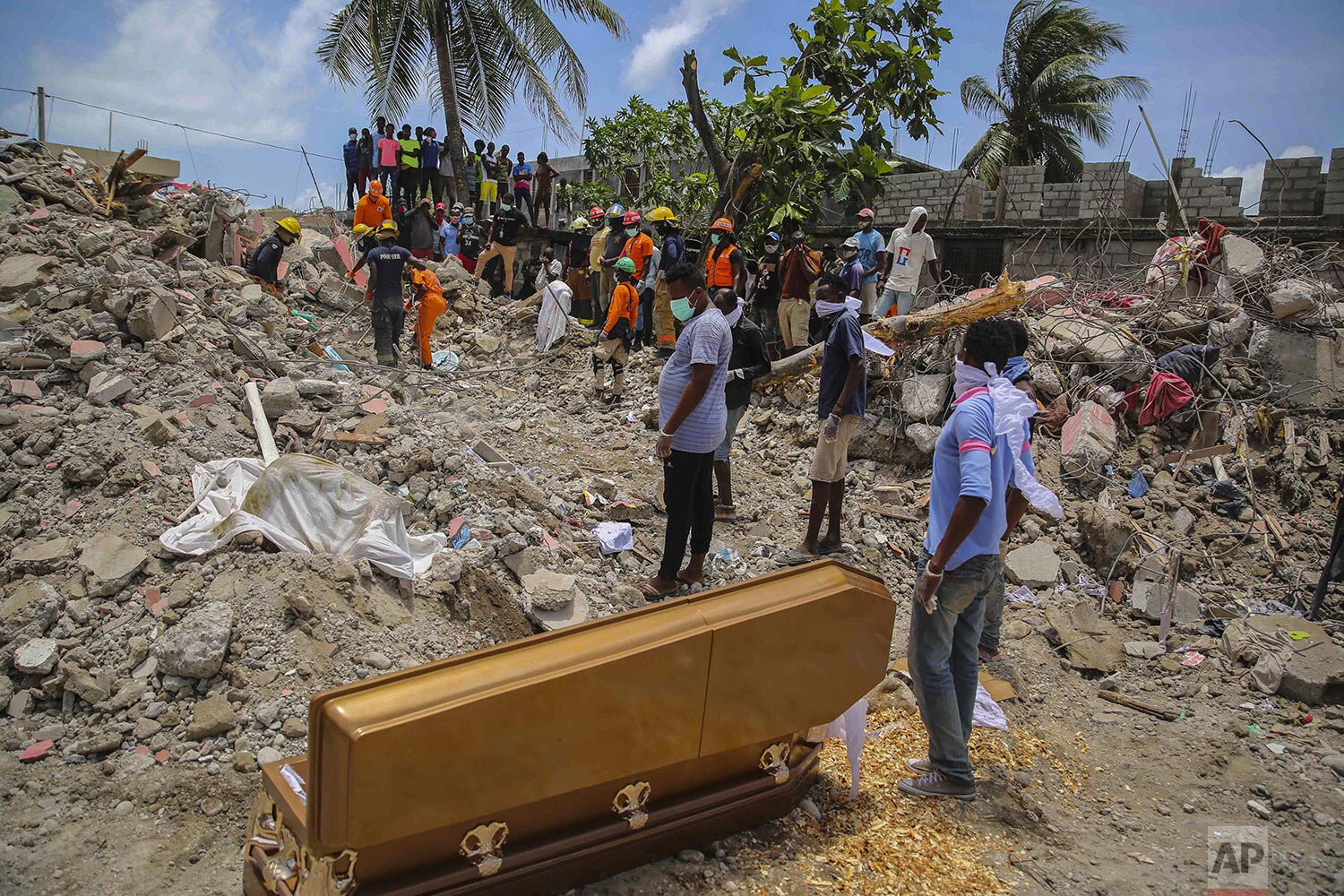  People stand next to an empty coffin near the sheet-covered remains of Francois Elmay whose body was recovered from the rubble of a home destroyed by the 7.2-magnitude earthquake in Les Cayes, Haiti, Aug. 18, 2021. (AP Photo/Joseph Odelyn) 