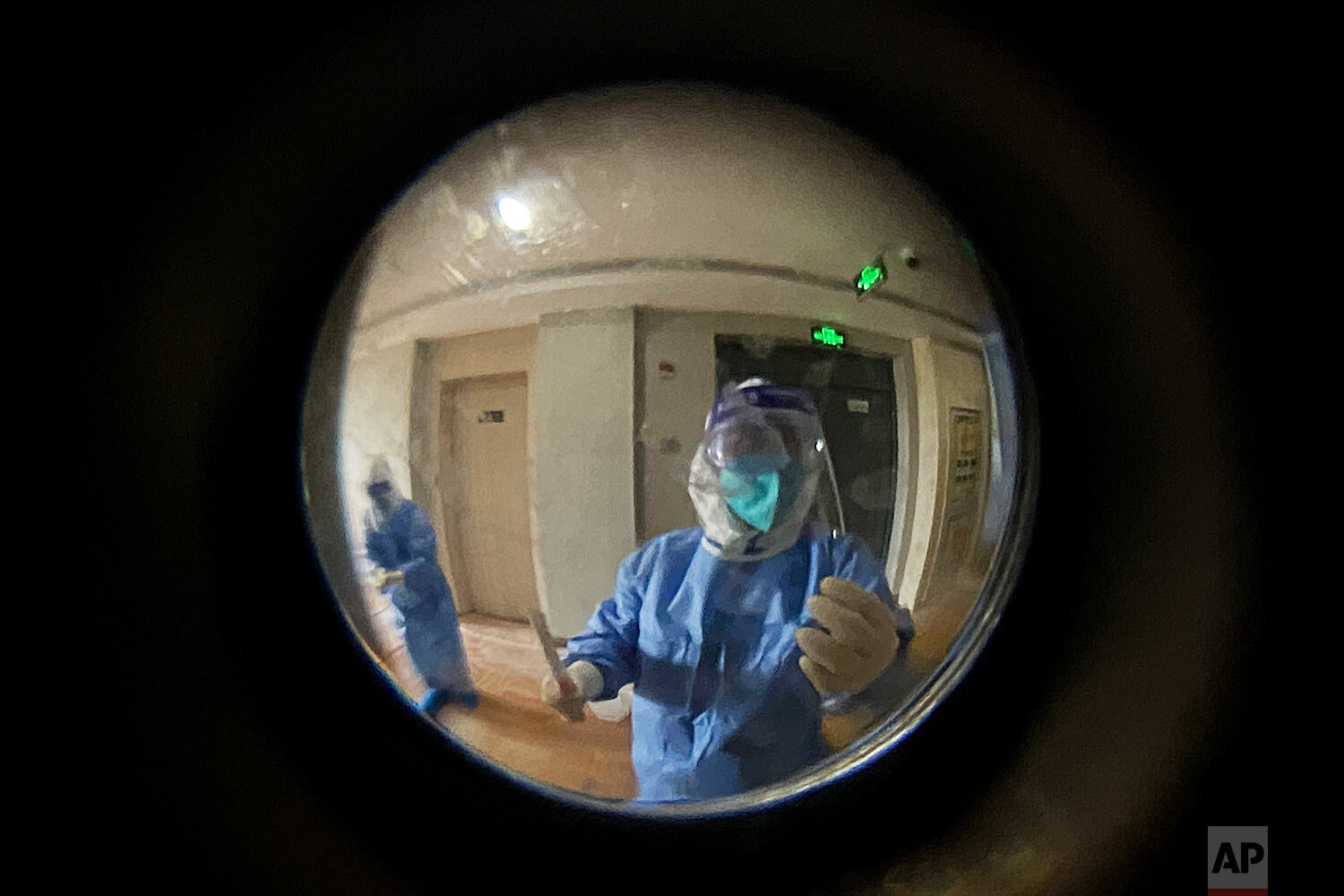  This photo taken through a door pinhole shows medical workers wearing a protective clothing prepares to take swab sample for the coronavirus test from an AP photographer during a period of health quarantine at a hotel in Shanghai, China, Thursday, A
