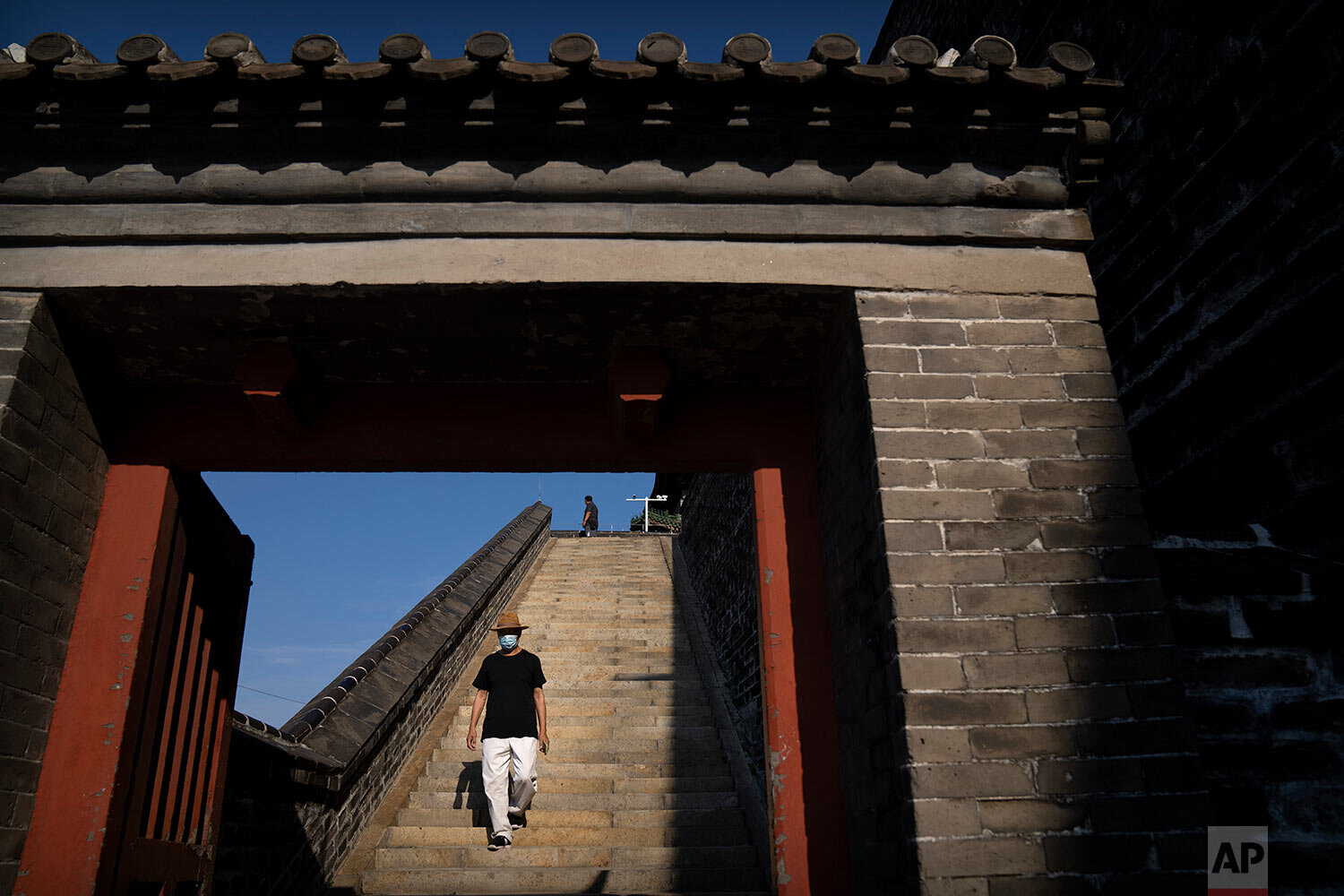  A man wearing a face mask to protect against COVID-19 walks down a flight of stairs at a park on a historic section of the old city wall in Beijing, Saturday, Aug. 28, 2021. (AP Photo/Mark Schiefelbein) 