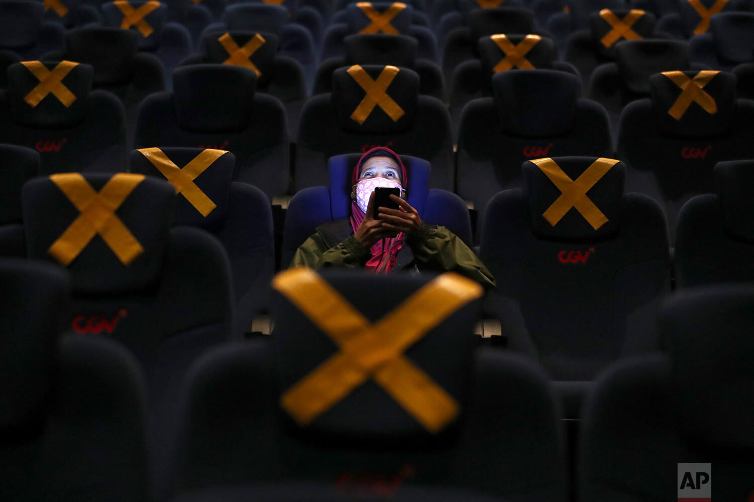  A customer uses her mobile phone before the start of a movie as she sits amid physical distancing markers during the first day of reopening at a cinema in Jakarta, Indonesia, Thursday, Sept. 16, 2021.  (AP Photo/Tatan Syuflana) 