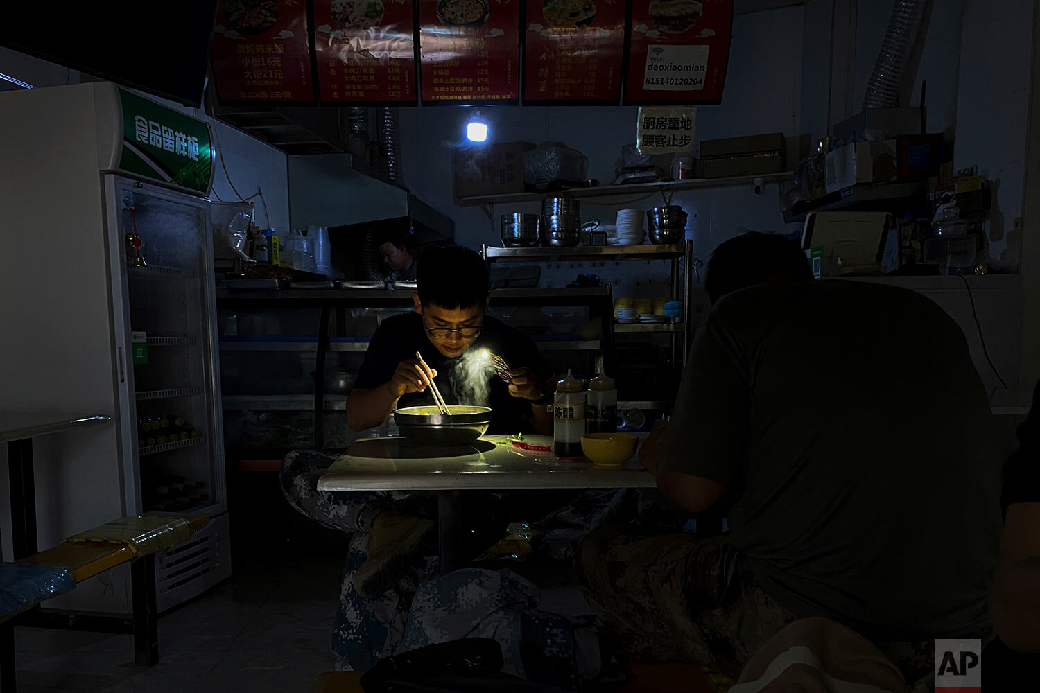  A man uses his smartphone flashlight to light up his bowl of noodles as he eats his breakfast at a restaurant during a blackout in Shenyang in northeastern China's Liaoning Province, Wednesday, Sept. 29, 2021. (AP Photo/Olivia Zhang) 