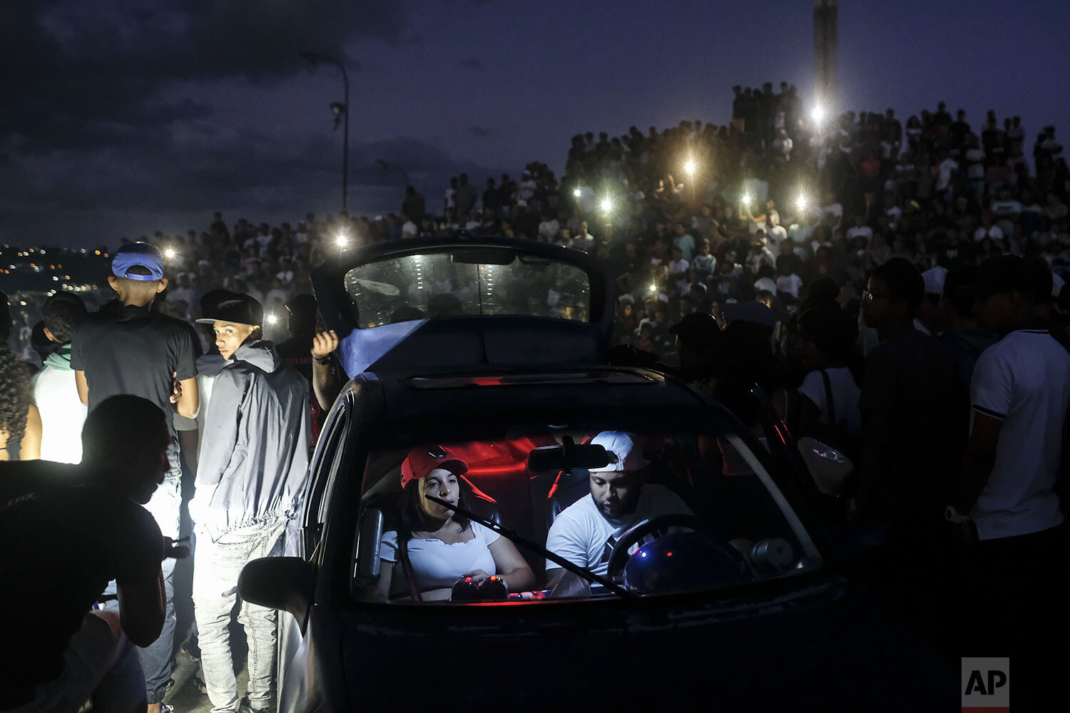  A couple turns on music in their car during a motorcycle stunt exhibition in the Petare neighborhood of Caracas, Venezuela, Sept. 26, 2021. (AP Photo/Matias Delacroix) 
