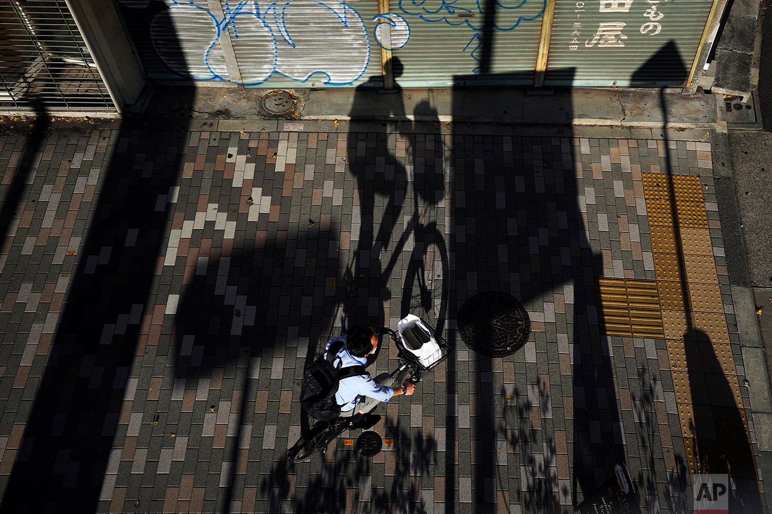  A long shadow from a bicyclist wearing a protective mask is cast on a sidewalk Monday, Oct. 11, 2021 in Tokyo. (AP Photo/Kiichiro Sato) 