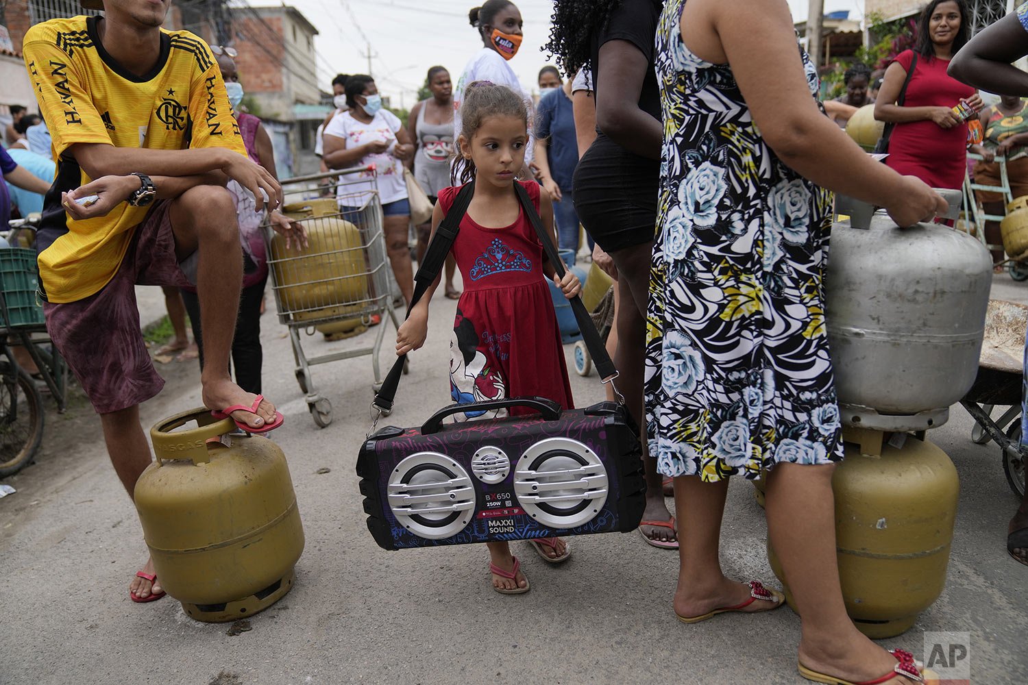 A girl carries a boom box playing music amid a crowd waiting to buy low cost cooking gas sold by the Petrobras Oil Tankers Union in the Vila Vintem favela of Rio de Janeiro, Brazil, Oct. 28, 2021. Soaring prices for gas, meat, electricity and more h