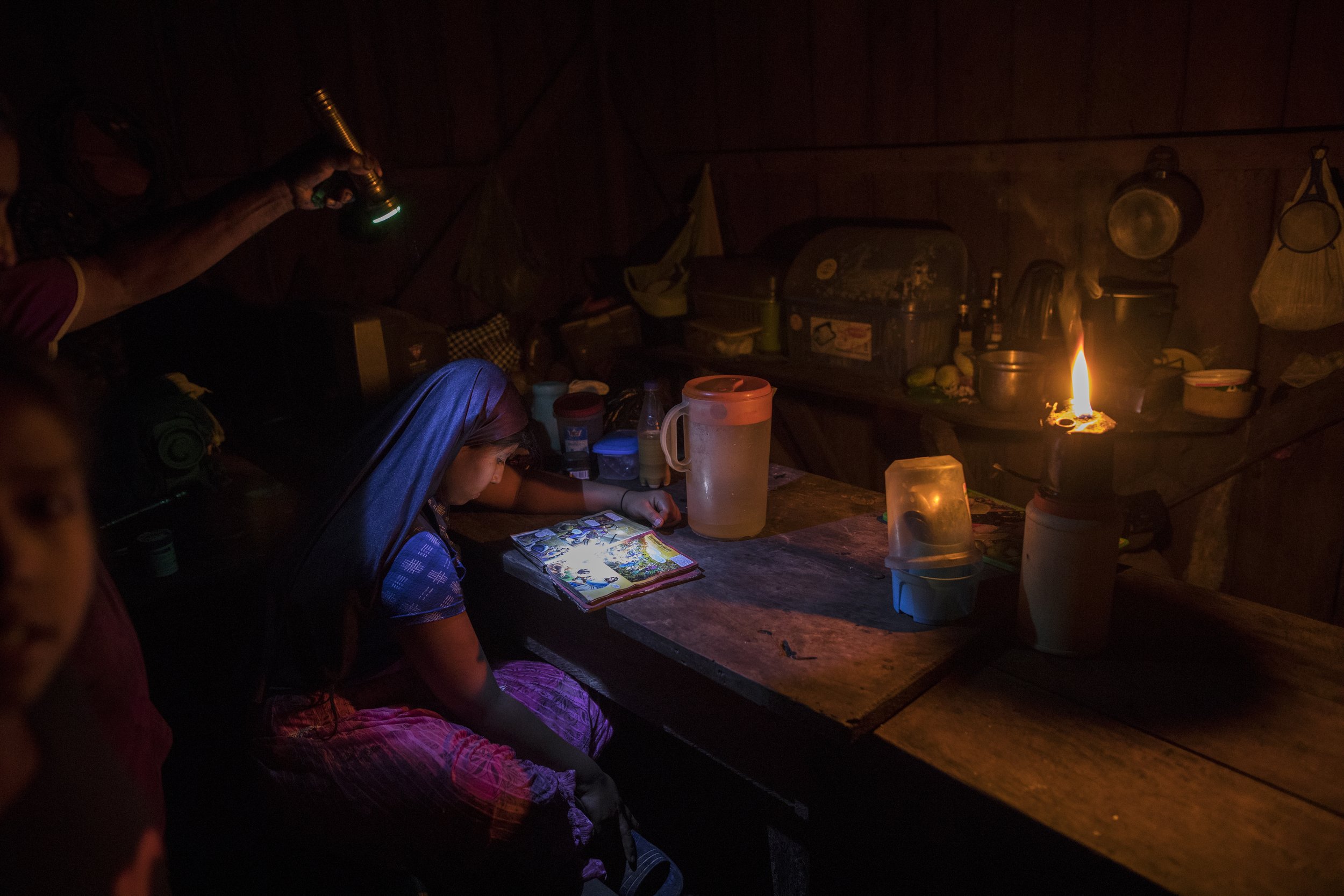  With the aid of a flashlight and a kerosene flame, 12-year-old Zairi Olivia, a member of the evangelical Christian sect Israelites of the New Universal Pact, looks at The Children's Illustrated Bible in her house in Jose Carlos Mariategui, Peru, a v
