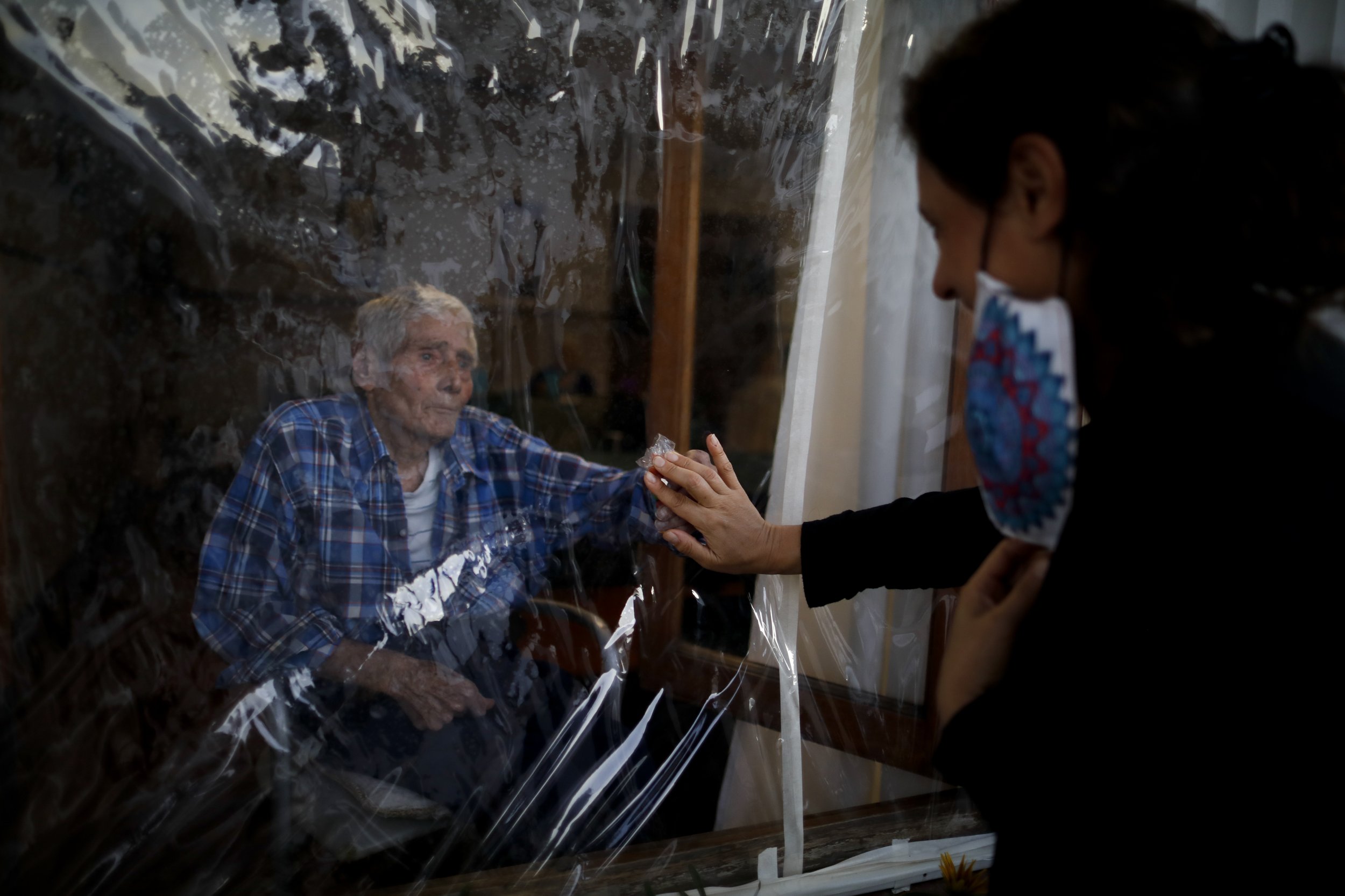  Victor Tripiana, 86, reaches out to touch the hand of his daughter-in-law, Silvia Fernandez Sotto, separated by a plastic sheet to prevent the spread of COVID-19, at the Reminiscencias residence for the elderly in Tandil, Argentina, on April 4, 2021