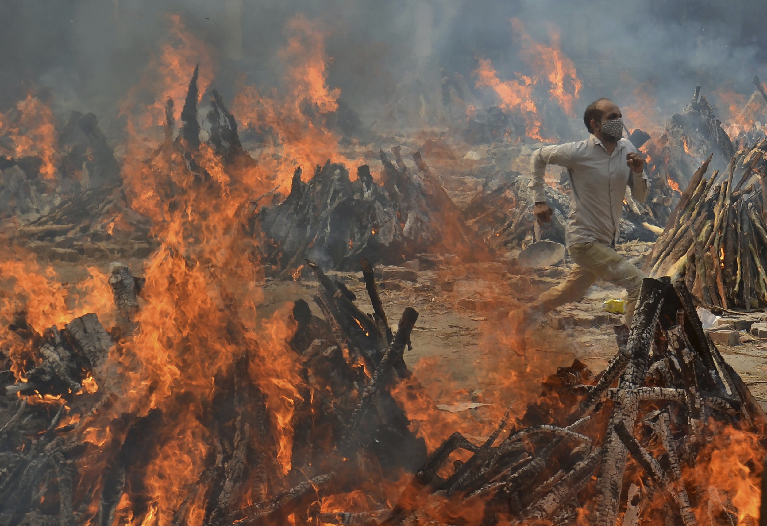  A man runs to escape the heat from multiple funeral pyres of COVID-19 victims at a crematorium on the outskirts of New Delhi, India, on April 29, 2021. (AP Photo/Amit Sharma) 