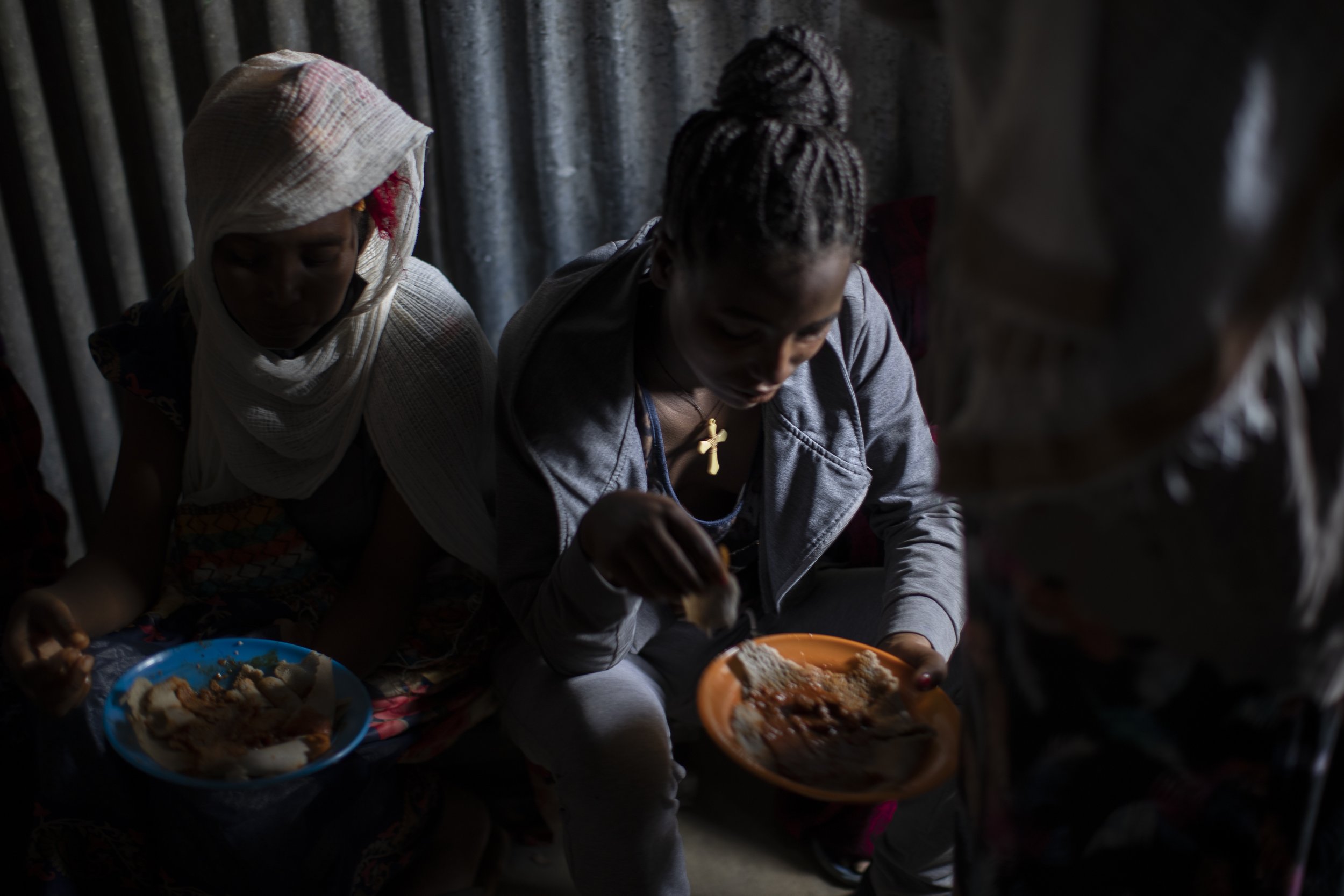  Displaced Tigrayan women, one wearing an Ethiopian Orthodox Christian cross, sit in a metal shack to eat food donated by local residents at a reception center for the internally displaced in Mekele, in the Tigray region of northern Ethiopia, on May 