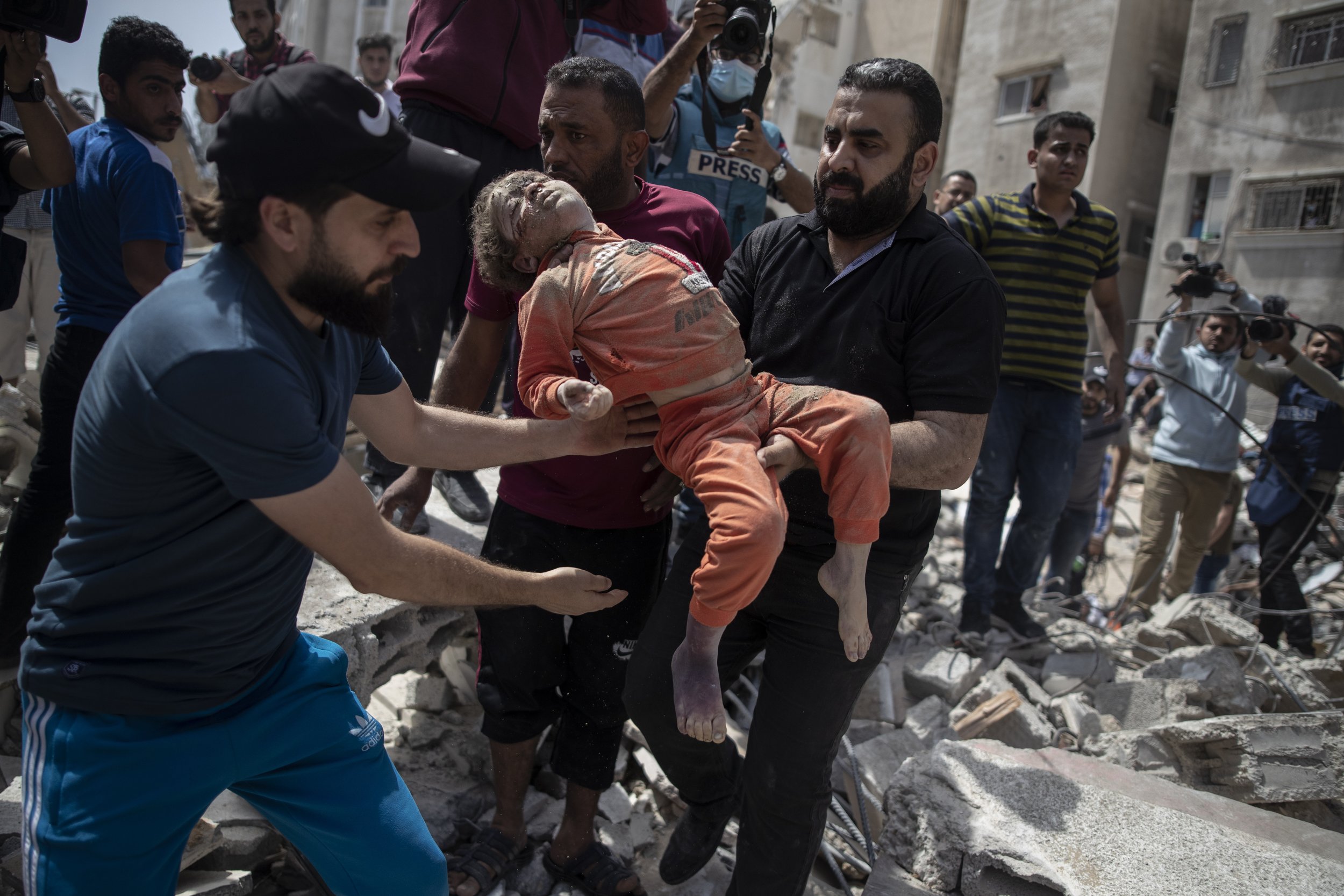  Men carry a dead child pulled from the rubble of a destroyed residential building in Gaza City following Israeli airstrikes on May 16, 2021, that flattened three buildings and killed at least two dozen people, according to medics. (AP Photo/Khalil H