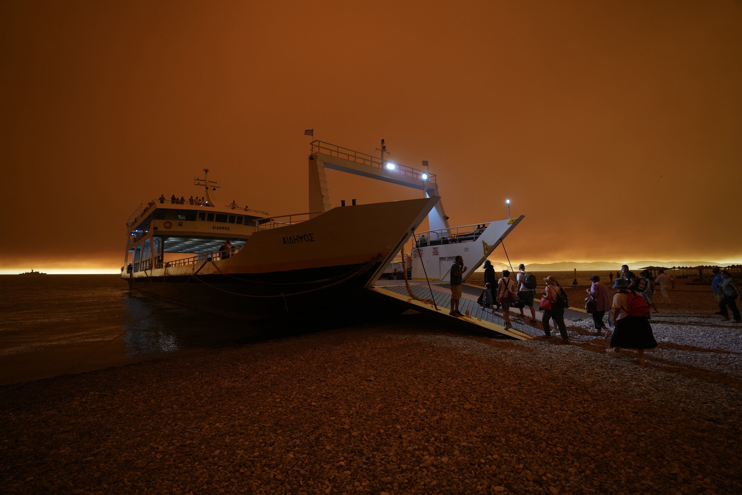  People board a ferry to evacuate from Pefki village on Evia island north of Athens, Greece, on Aug. 8, 2021, as a wildfire devours pristine forests on the island and smoke and ash block out the sun. (AP Photo/Petros Karadjias) 