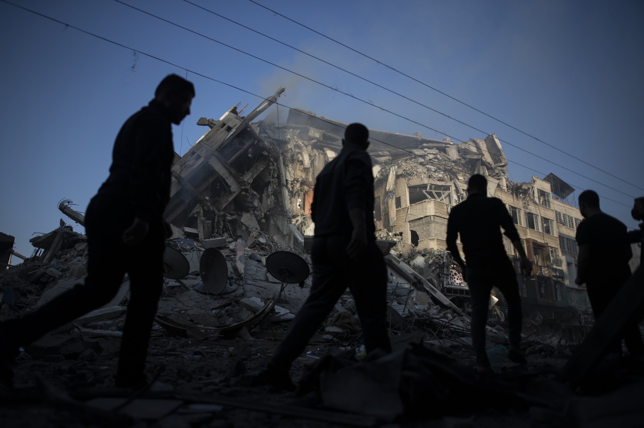  Palestinians walk past the remains of a 15 story building that was destroyed by Israeli airstrikes in Gaza City, on May 13, 2021. (AP Photo/Khalil Hamra) 