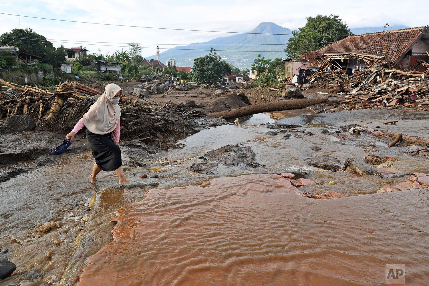 A woman makes her way through a damaged neighborhood following a flash flood in Bulukerto village, Batu, East Java, Indonesia, Friday, Nov. 5, 2021.  (AP Photo/Trisnadi) 