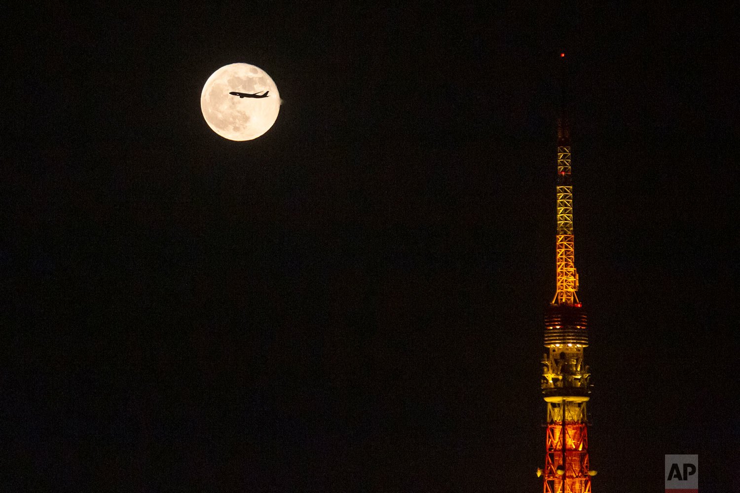 An airplane flies past the moon rising over Tokyo Tower Saturday, Nov. 20, 2021, in Tokyo. (AP Photo/Kiichiro Sato) 