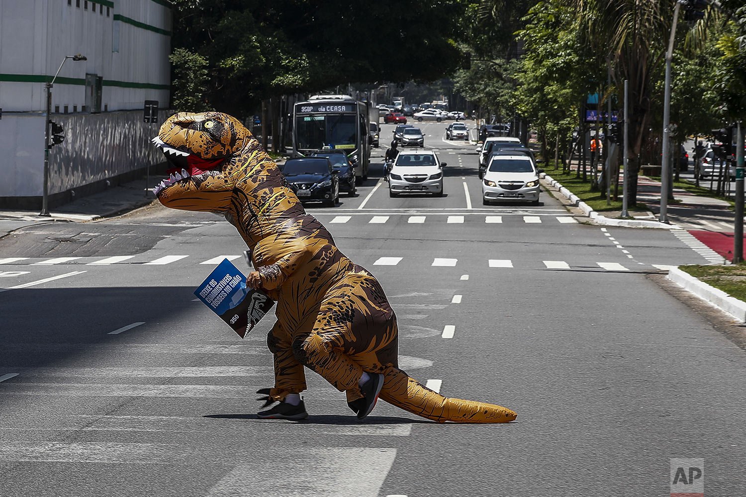  An activist wearing a dinosaur costume carries a sign that reads in Portuguese "Leave fossil fuels in the ground," during a protest demanding banks stop giving loans to companies involved in gas and oil development in the Amazon, in Sao Paulo, Brazi
