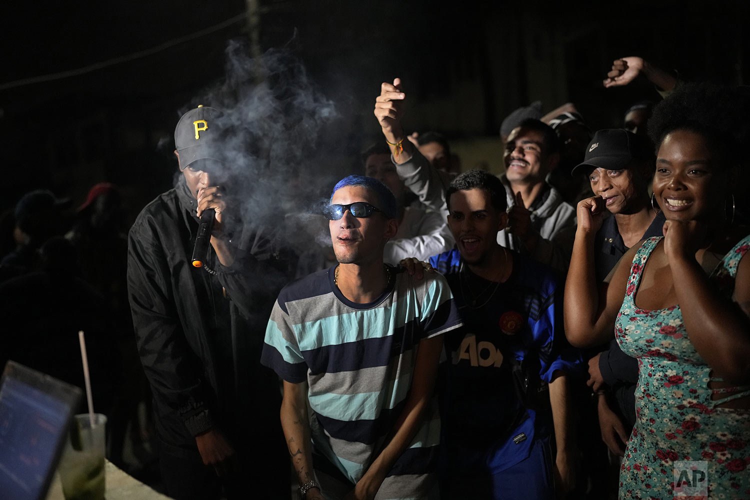  Rap artist Kunk, center, listens to a competitor at the Gas Battle rapping competition outside a bar in the City of God favela of Rio de Janeiro, Brazil, Nov. 10, 2021. (AP Photo/Silvia Izquierdo) 