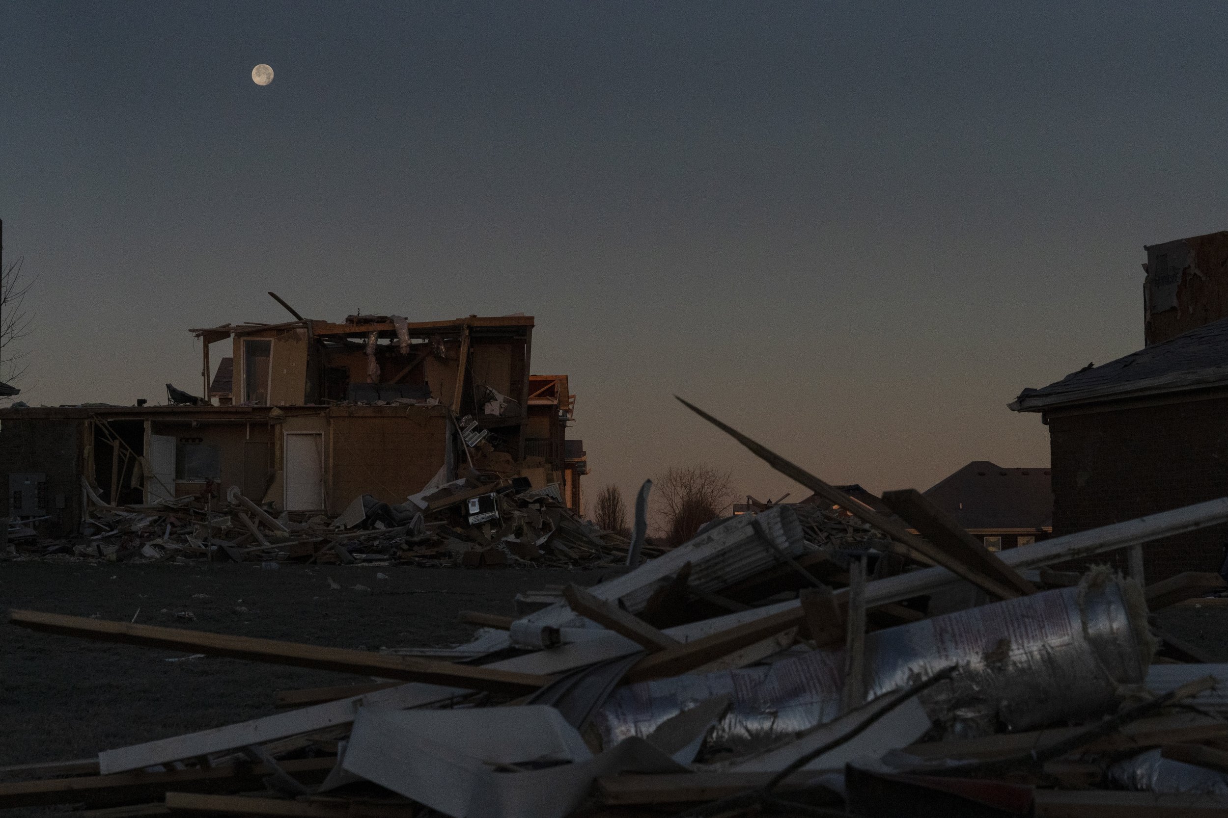  The moon sets as the first light of day reveals piles of debris and damaged homes in Bowling Green, Ky., Dec. 20, 2021. (AP Photo/Brynn Anderson) 