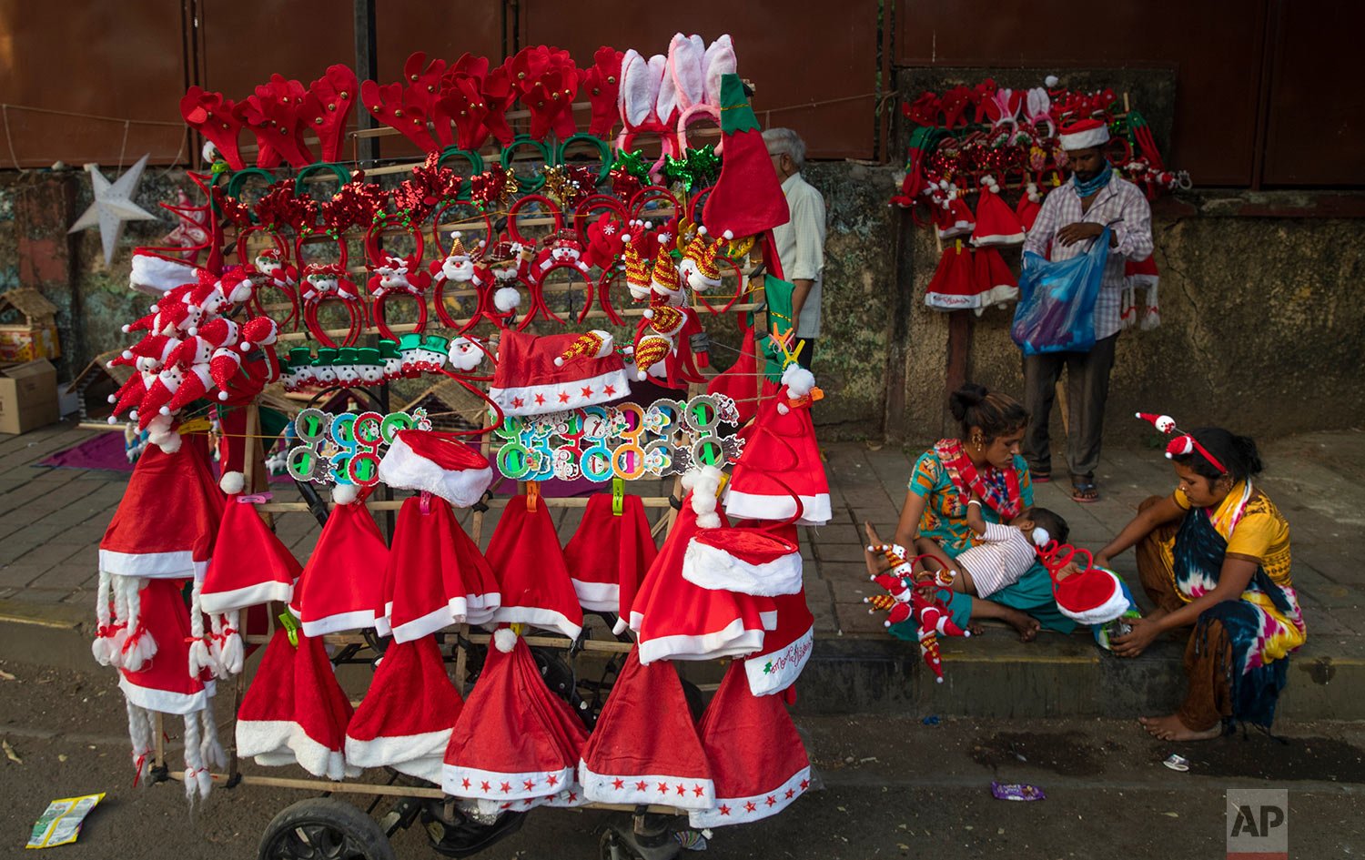  A woman feeds her child on the side of a road, as she waits for customers to buy decorative items for Christmas from her mobile shop, in Mumbai, India, Thursday, Dec. 23, 2021. (AP Photo/Rafiq Maqbool) 