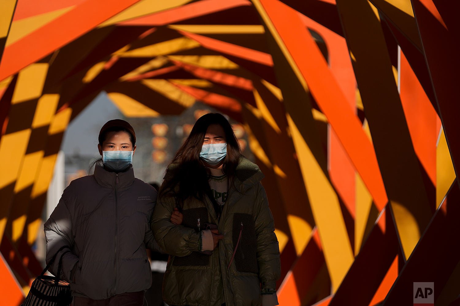  Women wearing face masks to help protect from the coronavirus walk by an art installation depicting a prosperity chamber on display outside a mall in Beijing, Monday, Dec. 27, 2021. (AP Photo/Andy Wong) 