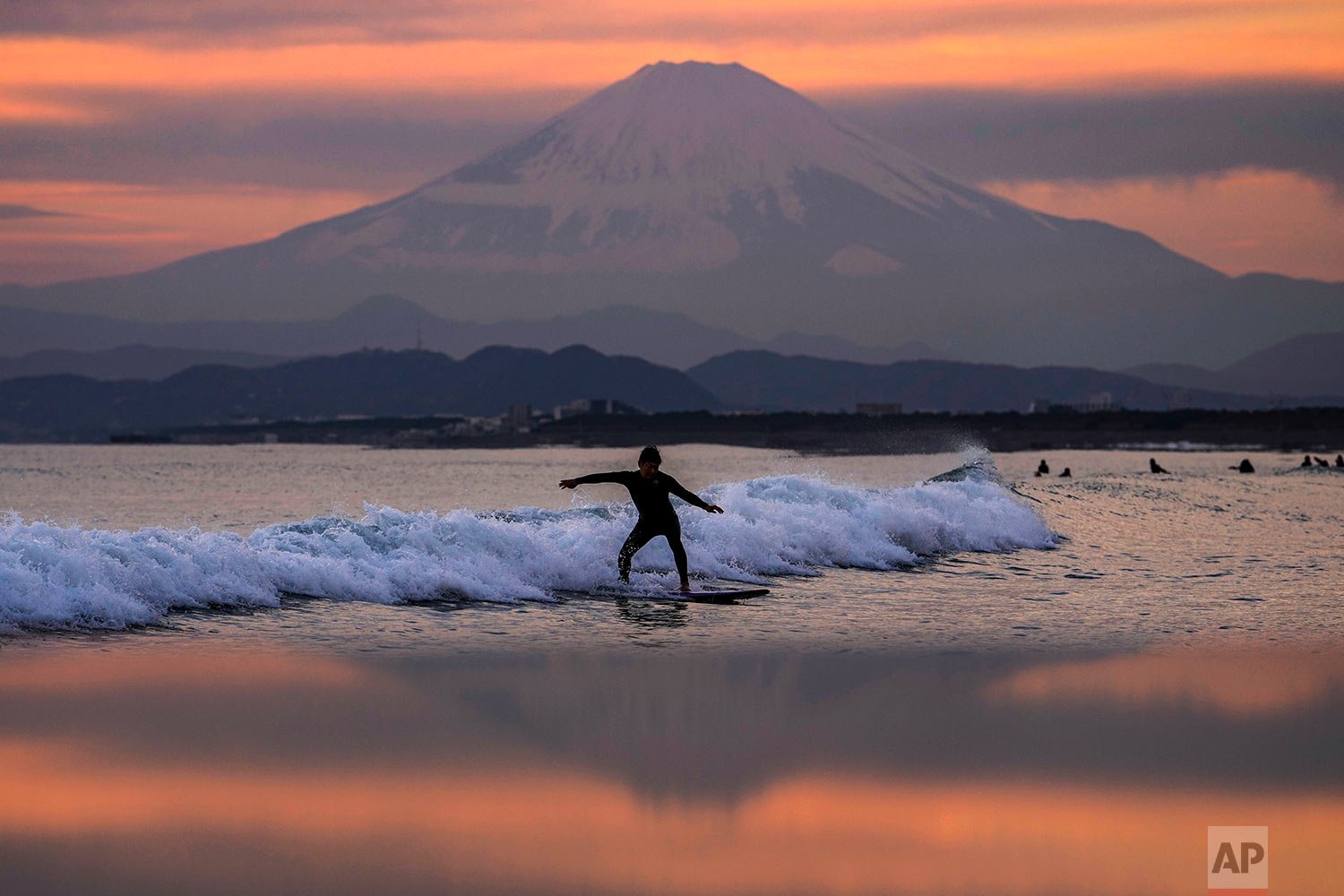  A surfer rides a wave in front of iconic Mount Fuji as the sun sets Friday, Dec. 10, 2021, in Fujisawa, south of Tokyo. (AP Photo/Kiichiro Sato) 